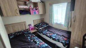 A compact bedroom with two beds, a small table, and a wardrobe.