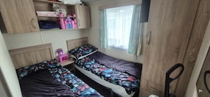 A compact bedroom with two beds, a small table, and a wardrobe.