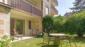 A two-story building with a balcony, a patio with a table and chairs, and a garden area with shrubs and flowers. - Apartment & Private Garden - Deauville-sevigne (Deauville)