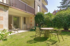 A two-story building with a balcony, a patio with a table and chairs, and a garden area with shrubs and flowers. - Apartment & Private Garden - Deauville-sevigne (Deauville)