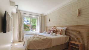 A bedroom with a large bed, a bedside table, a window with curtains, and a wall-mounted TV. - Apartment & Private Garden - Deauville-sevigne (Deauville)