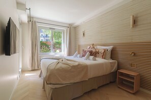 A bedroom with a large bed, a bedside table, a window with curtains, and a wall-mounted TV. - Apartment & Private Garden - Deauville-sevigne (Deauville)