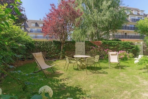 A garden with a table and chairs, surrounded by greenery and a building in the background. - Apartment & Private Garden - Deauville-sevigne (Deauville)