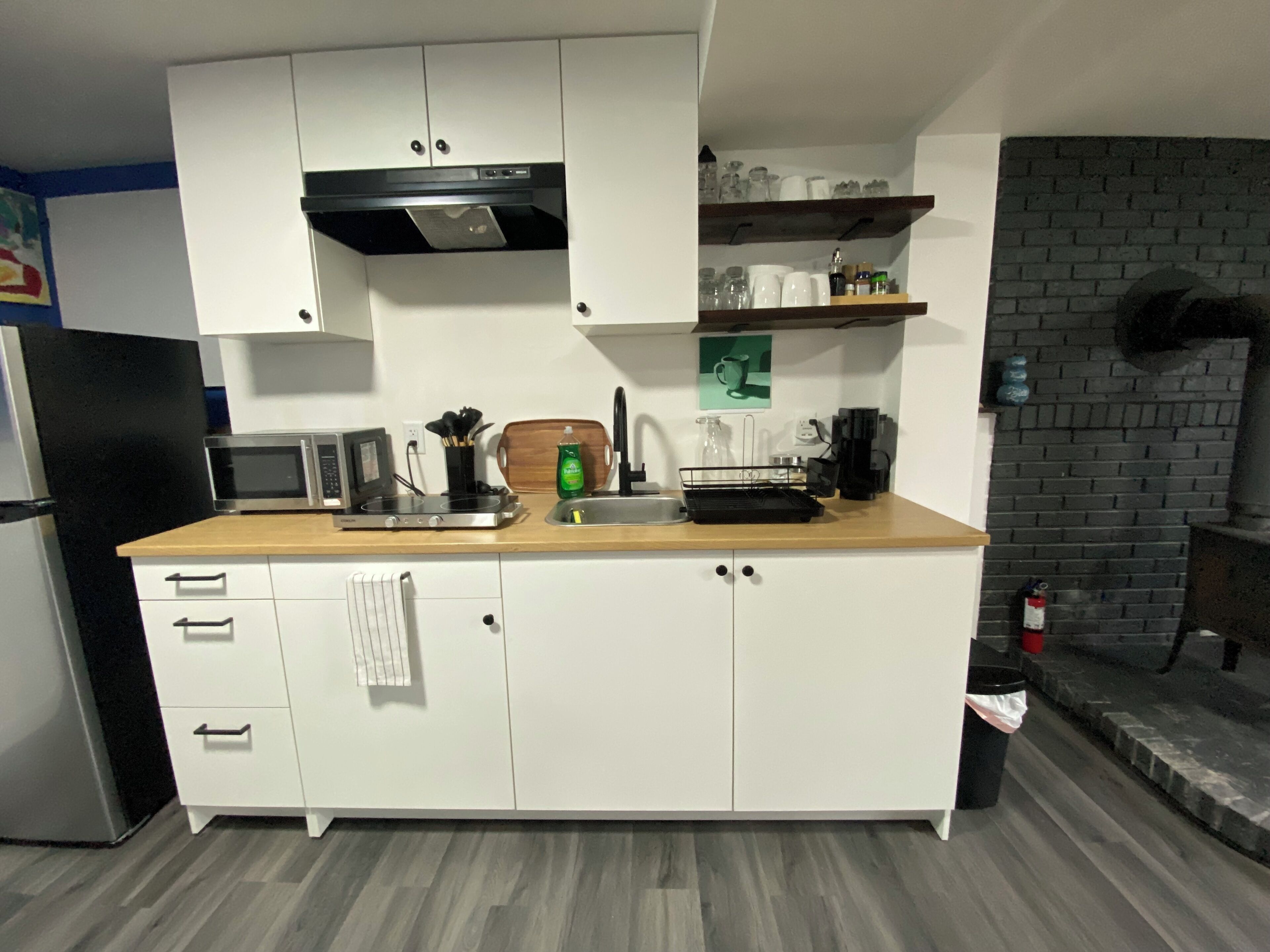 A modern kitchen with white cabinets, a microwave, a kettle, and a coffee machine.