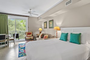 A hotel room with a bed, two lamps, a sofa, a chair, a balcony with a table and chairs, and a ceiling fan. - 🏖️Cozy Studio | Resort Pool + 2 Hot Tubs | Lasata 3315🏖️ (Miramar Beach)