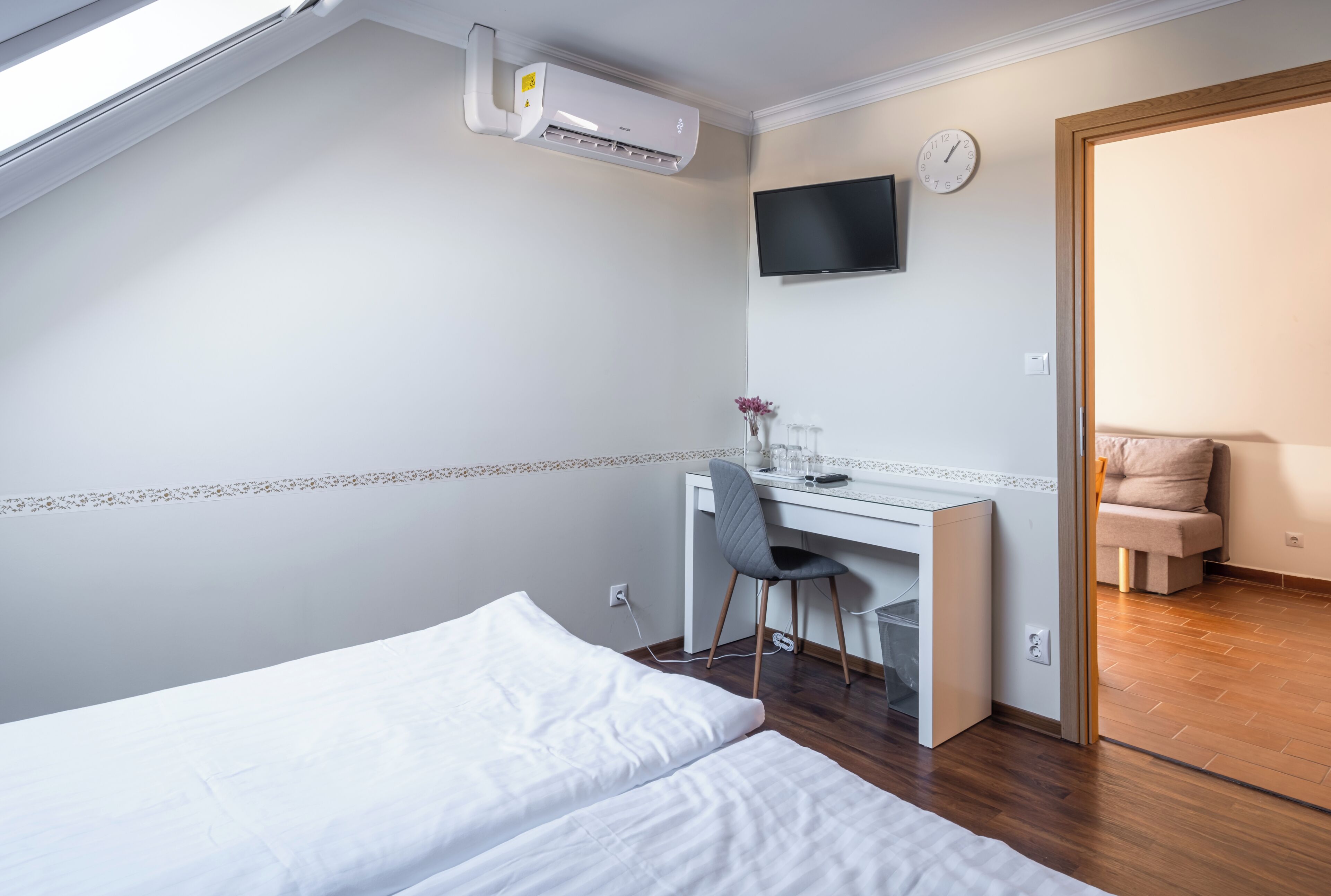 Un dormitorio con una cama, un escritorio, una silla, un televisor y un reloj en la pared.
