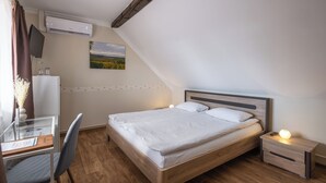 Un dormitorio con cama de madera, un escritorio con silla, aire acondicionado y un cuadro en la pared.