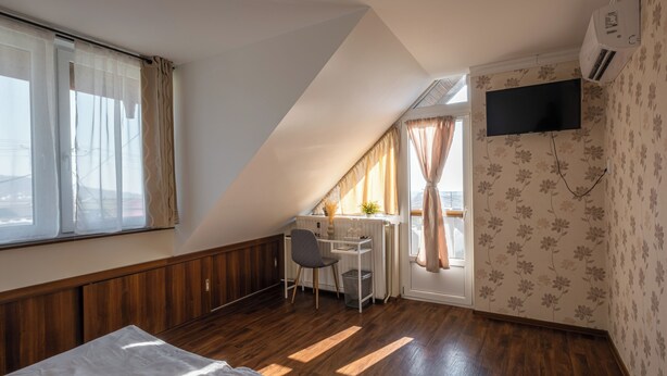 Un dormitorio con techo inclinado, una cama, un escritorio y un televisor montado en la pared.