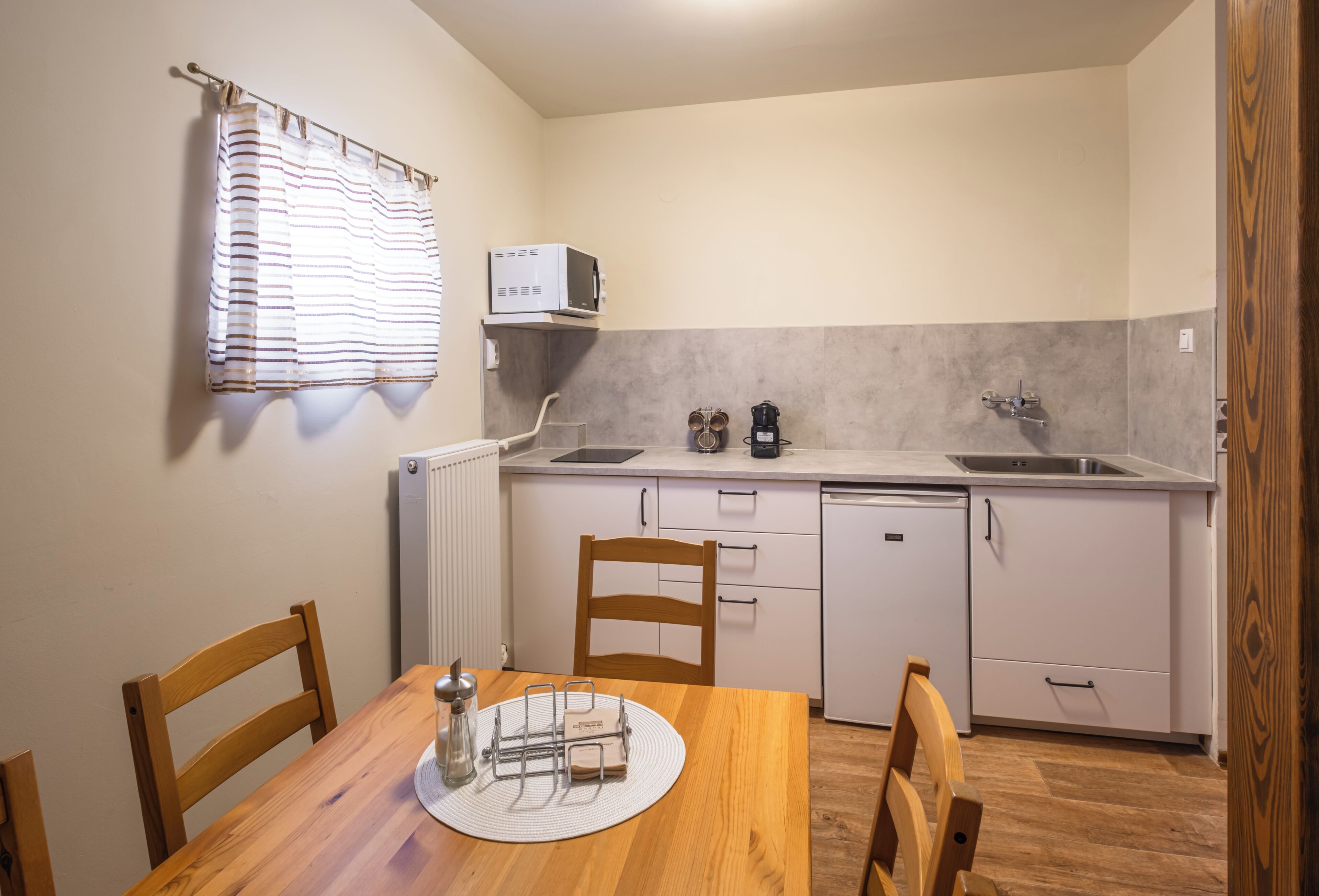 A compact kitchen with a dining table, chairs, a microwave, a kettle, and a sink.