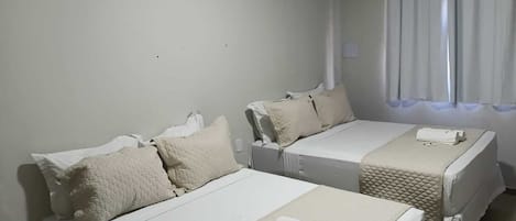 Habitación de hotel con dos camas individuales, ventana con cortinas, aire acondicionado y una pequeña mesa con toallas.