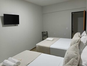 A hotel room with two beds, a television mounted on the wall, and a door leading to another room. - Amalfi Suites Pousada (João Pessoa)