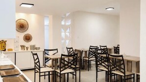 Un moderno comedor con varias mesas y sillas, una cocina con mostrador y electrodomésticos, y decoración mural.