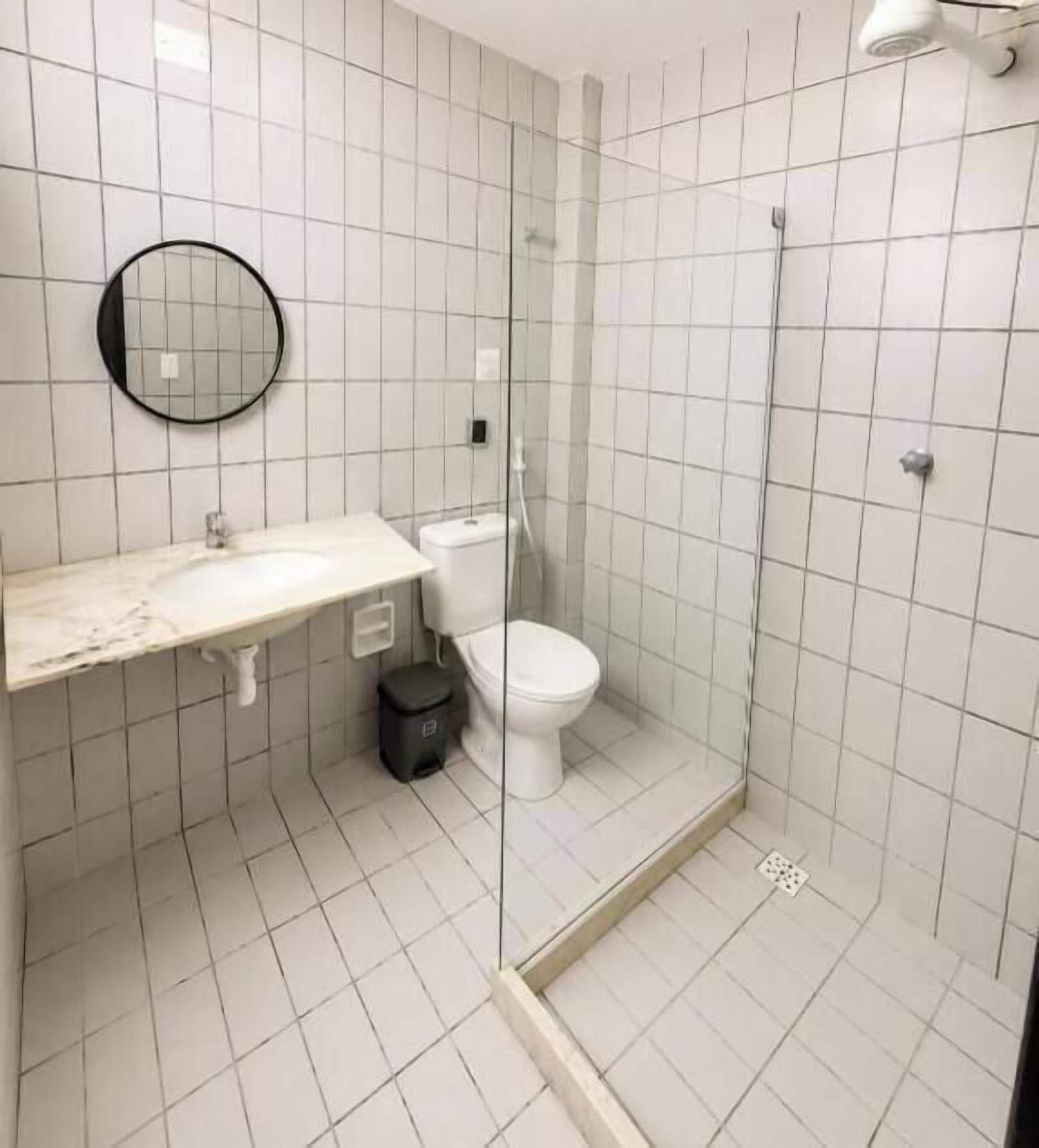 Un baño con ducha de vidrio, inodoro y lavamanos con espejo.