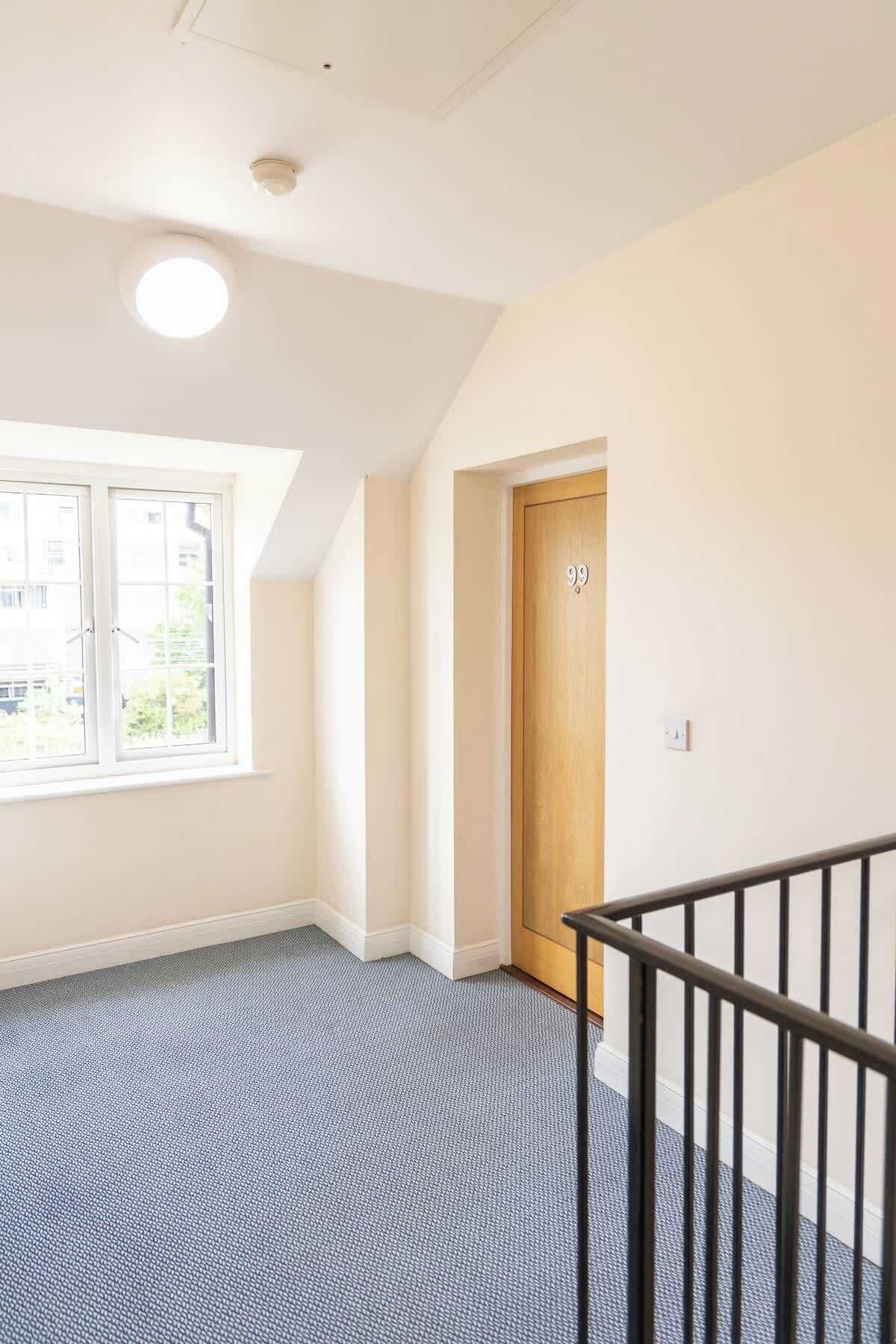 A room with a large window, a door with a number, and a staircase with a railing.