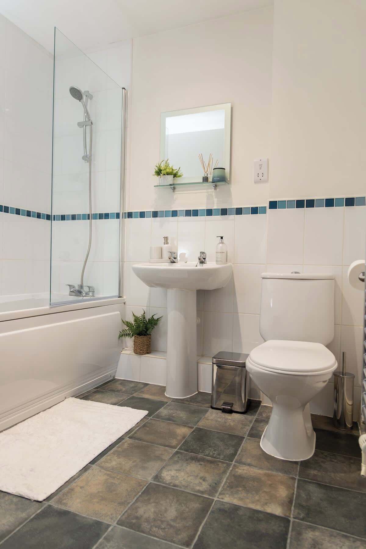 Bany amb dutxa de vidre, un lavabo, un vàter i una paperera petita.