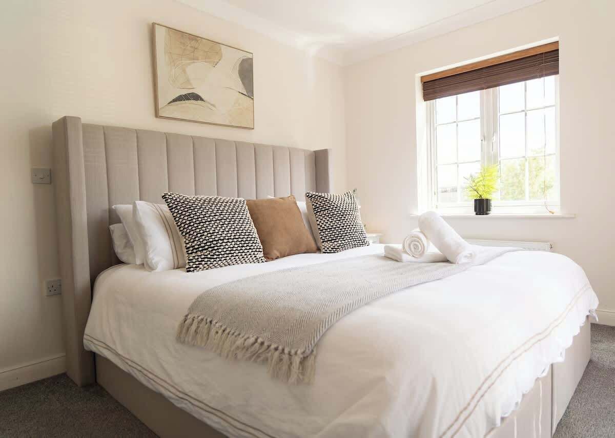 A neatly made bed with a grey headboard, white bedding, and patterned pillows.