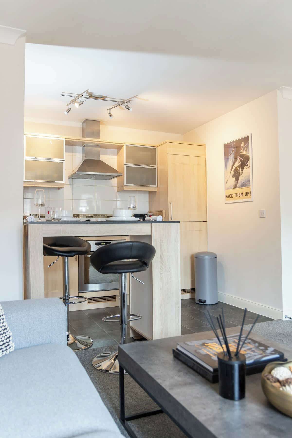 A modern kitchen with a central island, bar stools, and a dining area with a sofa.