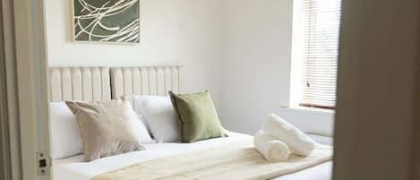 A bedroom with a bed, pillows, a blanket, a wall art piece, and a window with blinds.
