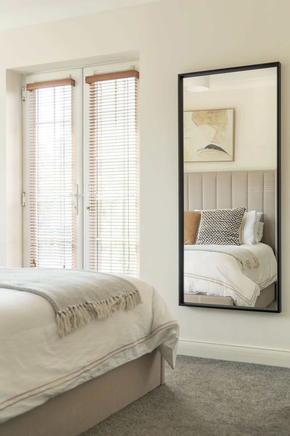 A bedroom with a bed, a large mirror, and a window with blinds.
