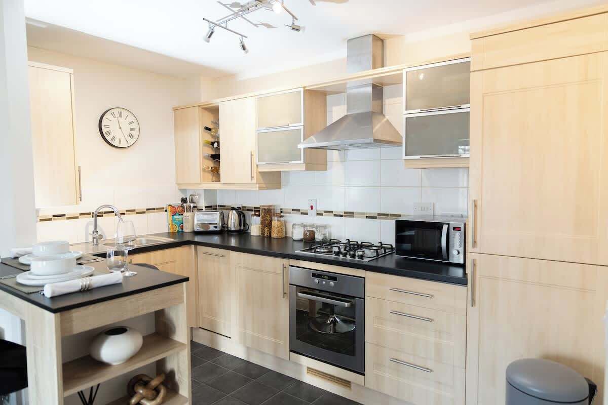 A modern kitchen with a gas stove, oven, microwave, and a clock on the wall.