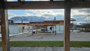 Ein Außenbereich mit einer Holzpergola, einem gepflasterten Weg und Gebäuden im Hintergrund.