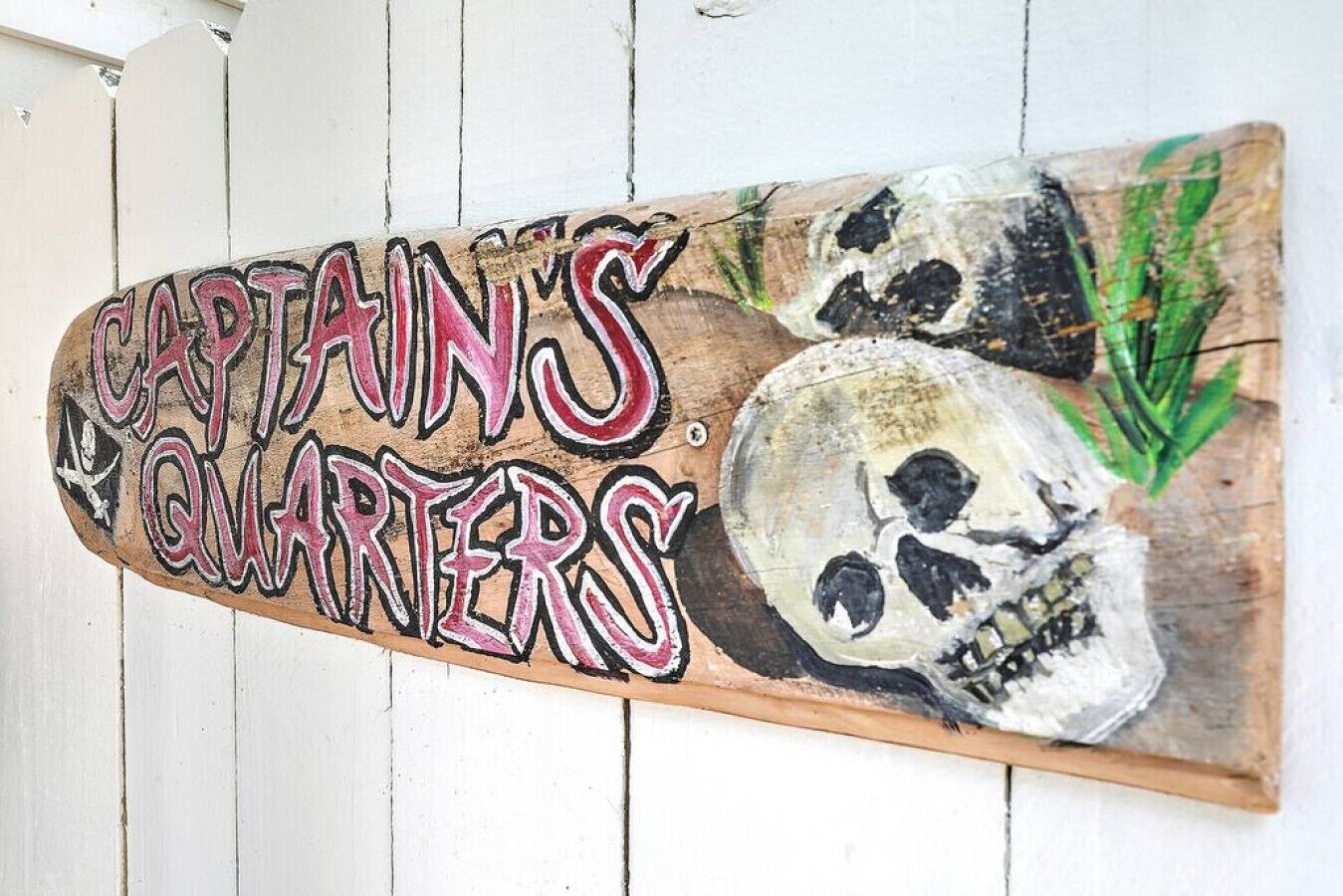 Un letrero de madera con el texto 'CAPTAIN'S QUARTERS' y un diseño de calavera.