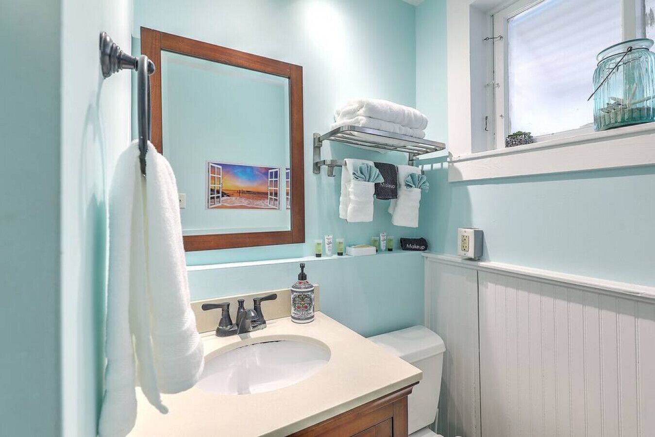 A bathroom with a white sink, a mirror, a towel rack, and a window with a view.