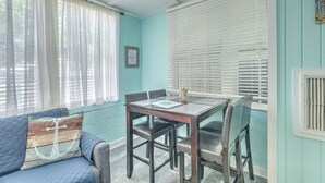 A room with a dining table and chairs, a blue sofa, and a window with white blinds. - “Captain`s Quarters” at Pirates Perch! (Folly Beach)