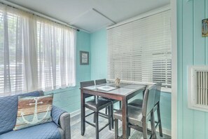 Ein Zimmer mit Esstisch und Stühlen, einem blauen Sofa und einem Fenster mit weißen Jalousien.