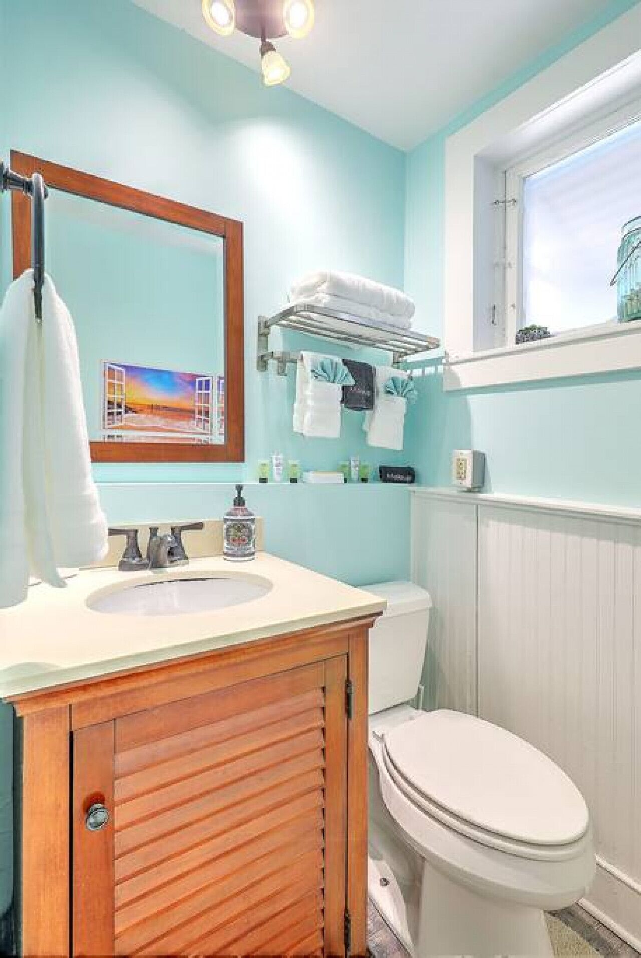 A bathroom with a wooden vanity, a sink, a toilet, and a window above the toilet.