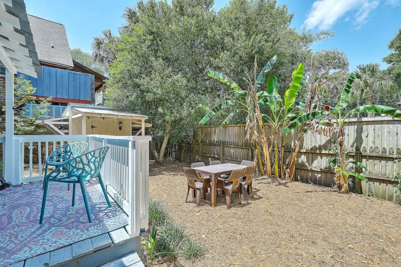 Un jardin avec une terrasse, une table et des chaises, et une clôture en bois.