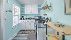 A kitchen with white cabinets, a countertop, and a wooden table. - “Captain`s Quarters” at Pirates Perch! (Folly Beach)
