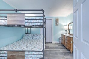Ein Stockbett mit gemustertem Bettbezug, eine Kommode mit Spiegel und eine Tür in einem Zimmer mit hellblauen Wänden.