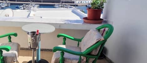 A balcony with a view of the sea, a table, two chairs, and a potted plant.