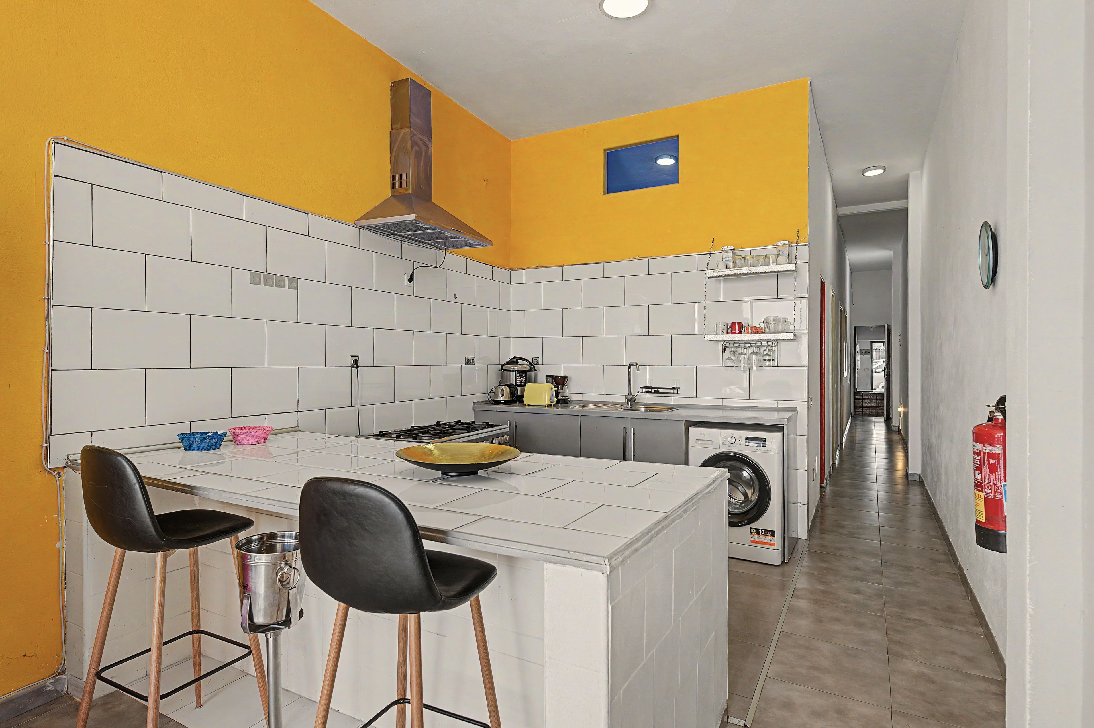 A compact kitchen with a central island, bar stools, a stove, and a washing machine.