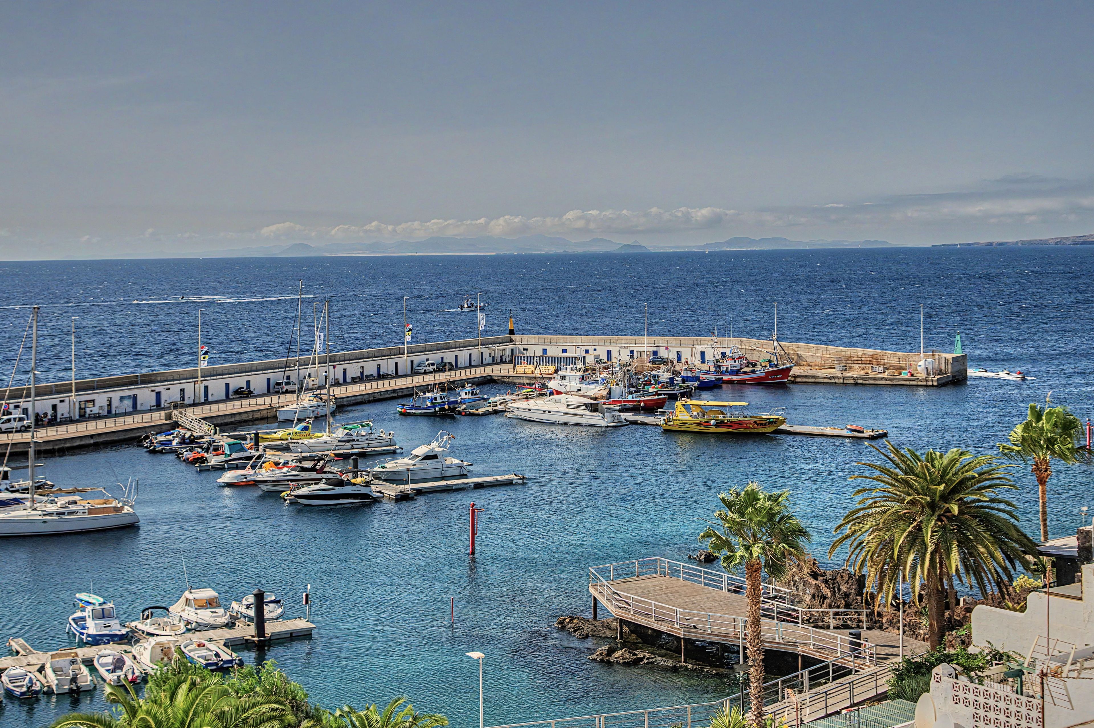 A marina with various boats docked, a pier extending into the water, and a rocky coastline in the background.