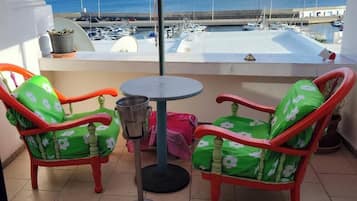 Ein Balkon mit zwei Stühlen und einem Tisch, der auf einen Yachthafen mit Booten blickt.