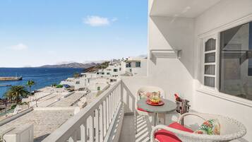 A balcony with a table and chairs, overlooking a coastal area with buildings and the sea.