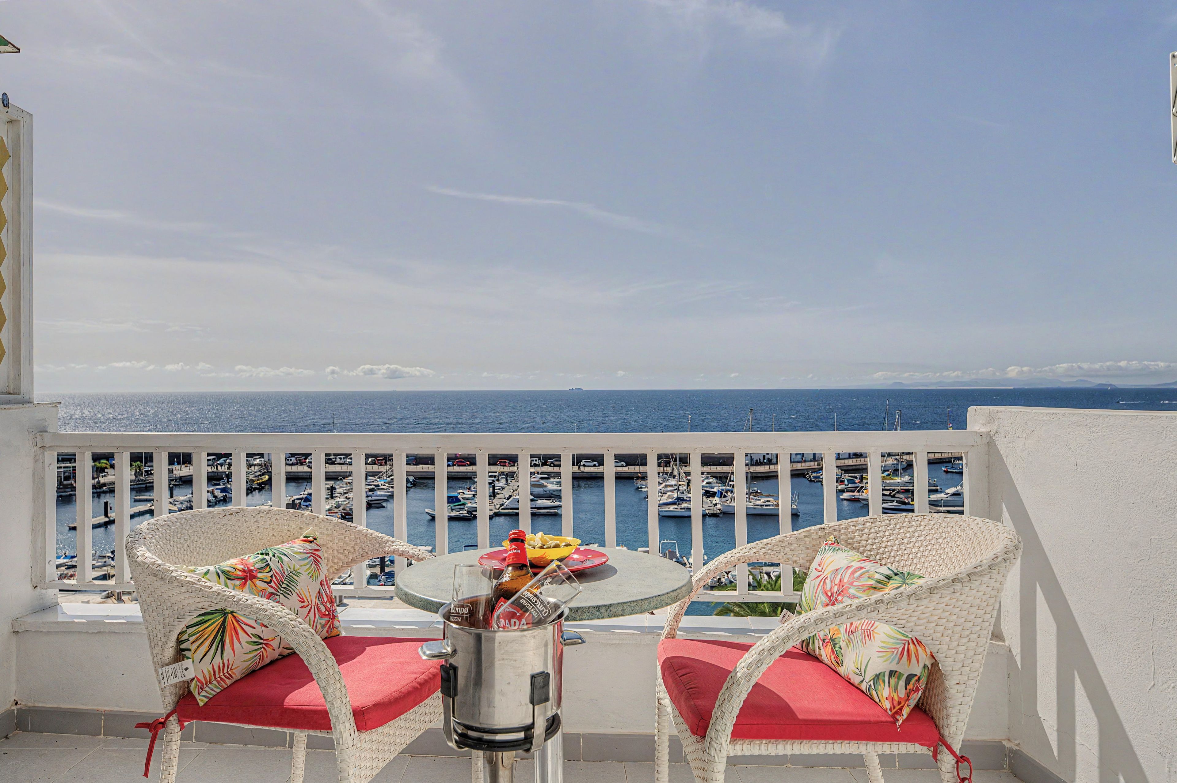 A balcony with wicker chairs and a table, overlooking a marina with boats.