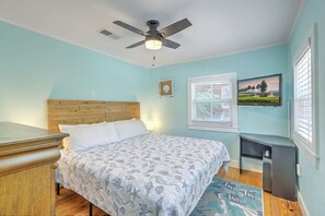 A bedroom with a bed, a ceiling fan, a window with blinds, a picture on the wall, and a small desk with a lamp. - `Pirates Perch` - Walkable to everything Folly! (Folly Beach)