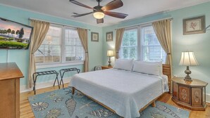 A bedroom with a bed, two bedside tables, a ceiling fan, and a window with curtains. - `Pirates Perch` - Walkable to everything Folly! (Folly Beach)