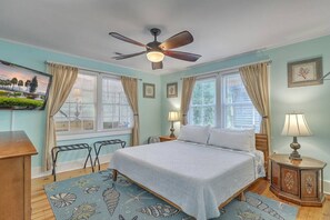 Ein Schlafzimmer mit einem Bett, zwei Nachttischen, einem Deckenventilator und einem Fenster mit Vorhängen.