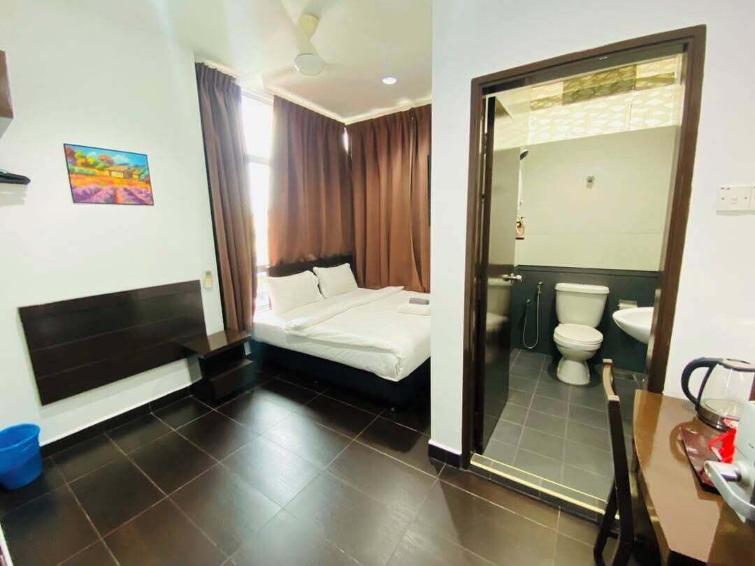A hotel room with a bed, a bathroom with a toilet and sink, and a small table with a chair.
