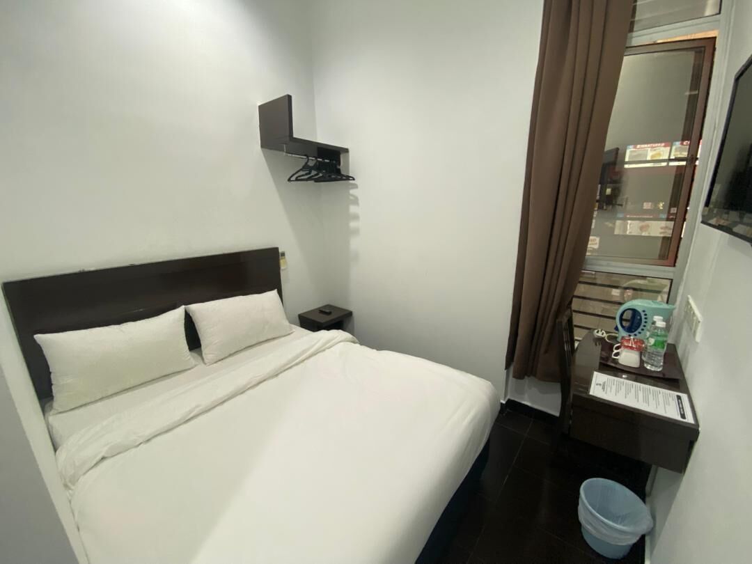 A hotel room with a bed, a nightstand, a mirror, a window with curtains, and a small table with a water bottle and a phone.