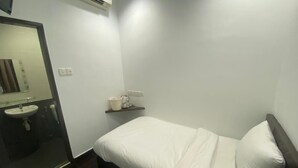 Una habitación pequeña y limpia con una cama, una mesita de noche, un espejo y un estante con artículos de tocador.
