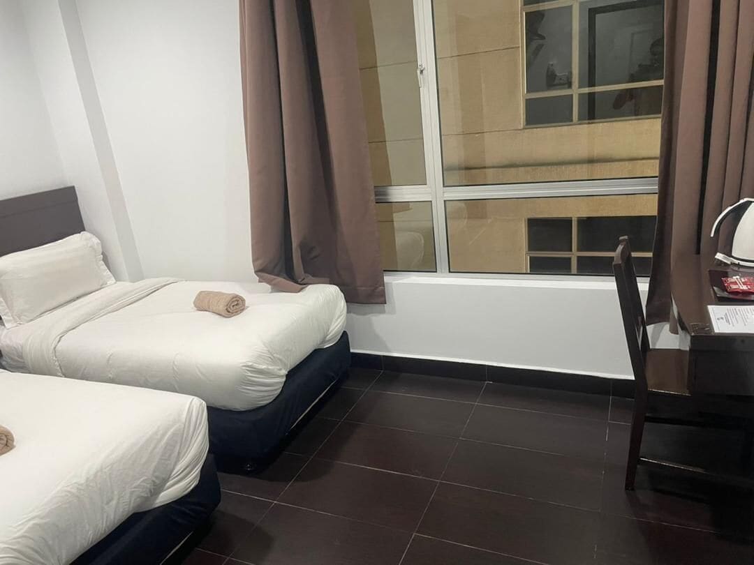 Habitación de hotel con dos camas, un escritorio y una ventana con cortinas.