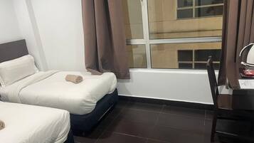 Habitación de hotel con dos camas, un escritorio y una ventana con cortinas.