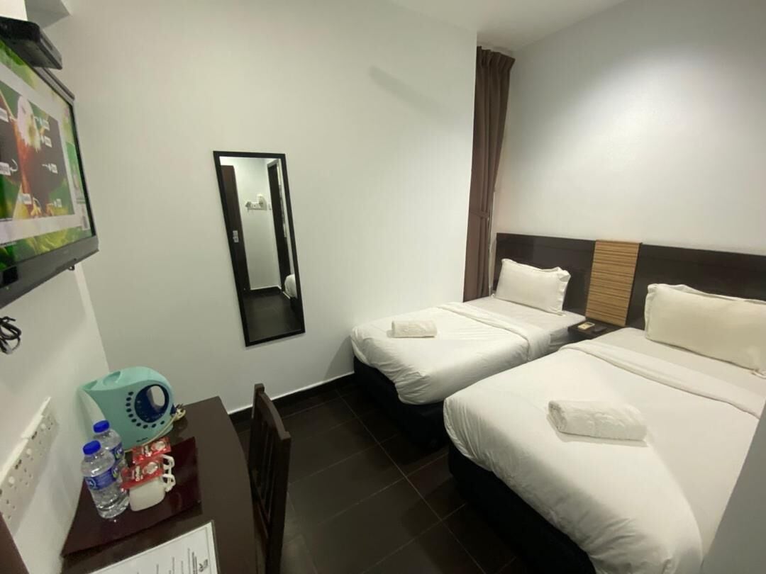 A hotel room with two beds, a mirror, a small table with a water bottle, and a TV on the wall.