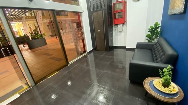 Un hall con una recepción, un sofá negro, una mesita con una planta y un reloj en la pared.