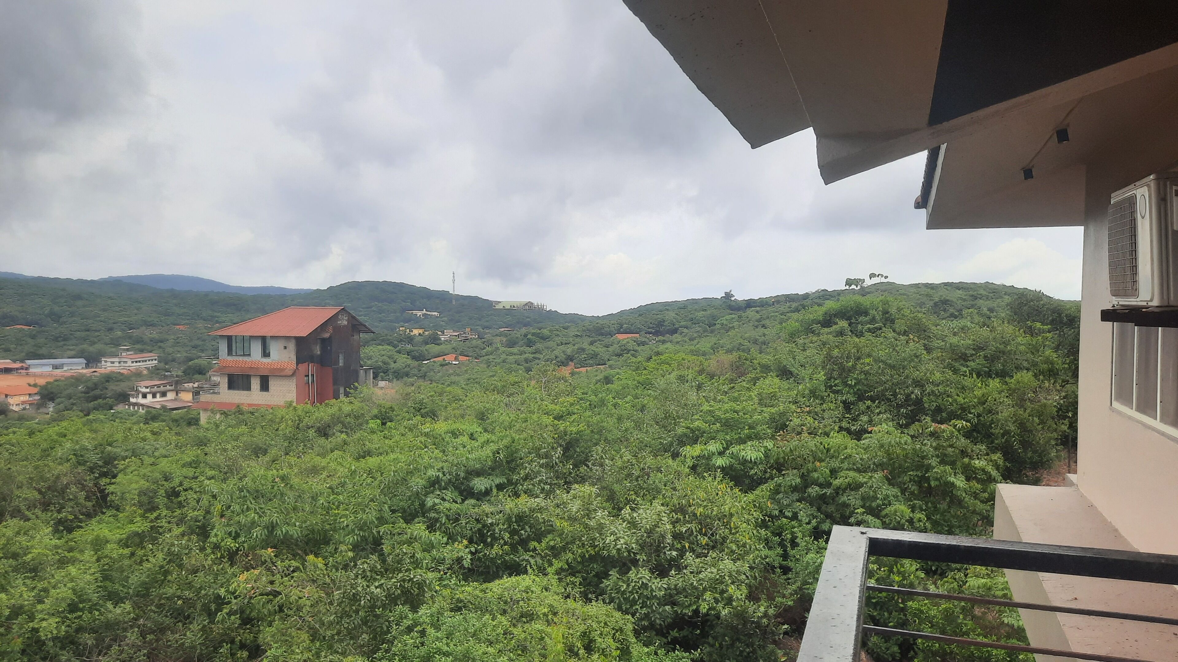A residential area with a house on a hill, surrounded by greenery and other buildings.
